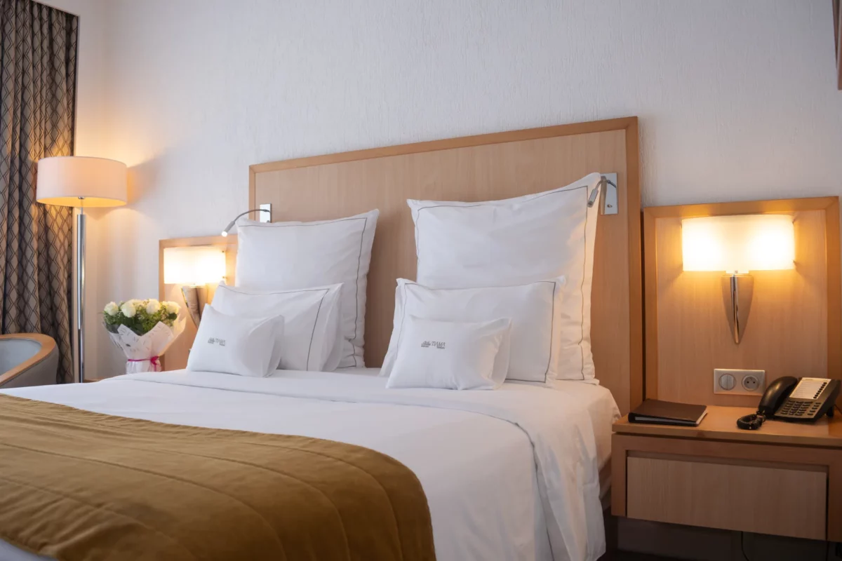 Chambre Standard de l'Hôtel TIAMA à Abidjan : lit double, tête de lit en bois et appliques murales